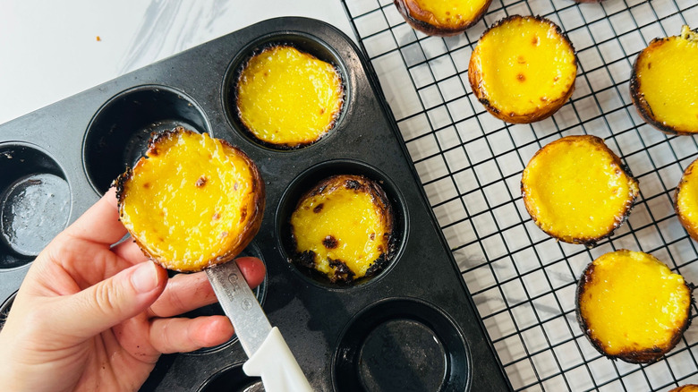 Hands removing custard tarts from muffin tin onto wire rack