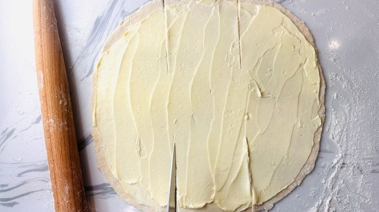 Rolled out dough coated in butter with slits cut in top and bottom