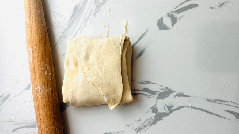 Dough square folded over onto itself next to rolling pin