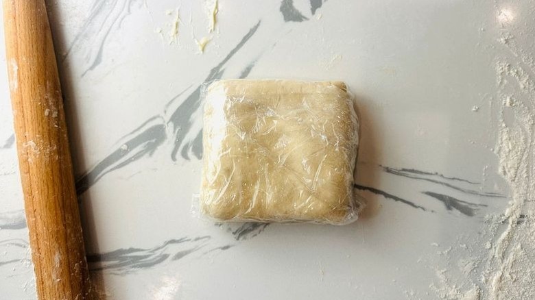 Dough square wrapped in plastic next to rolling pin