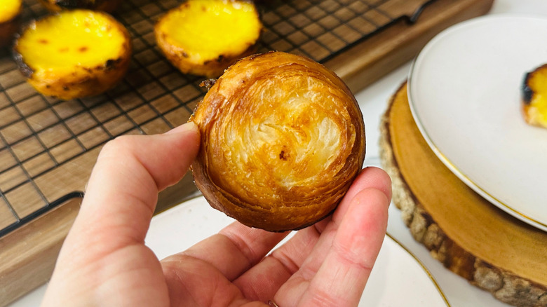 Hand holding custard tart upside down to show browned pastry crust