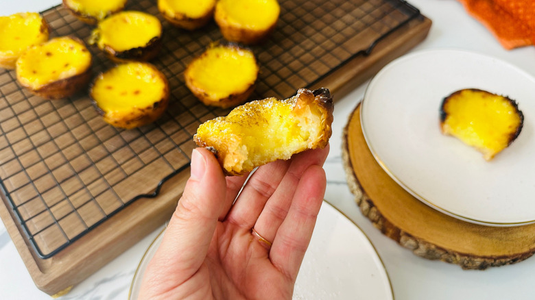 Hand holding custard tart with bite taken