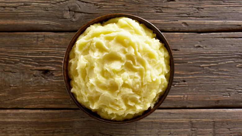 A bowl of mashed potatoes on a wooden table.