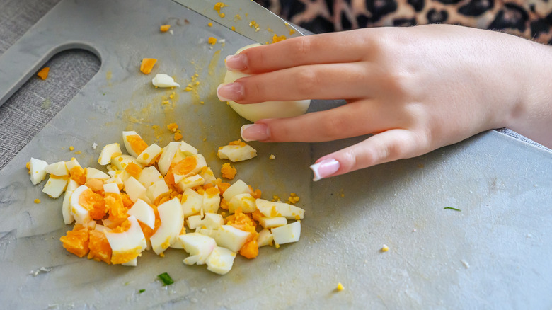Hands chopping hard-boiled egg with a knife on a cutting board for meal preparation
