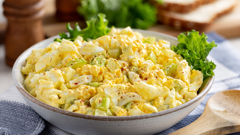 Egg salad in a bowl with bread slices and lettuce on a cutting board in background