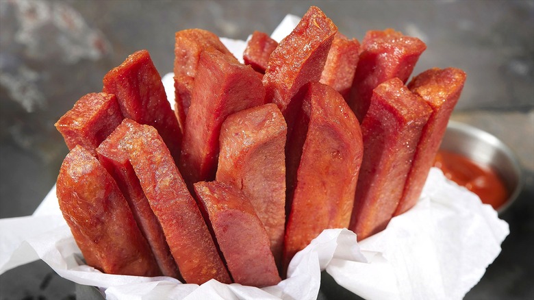 Crispy Spam fries in a serving container surrounded by white food paper