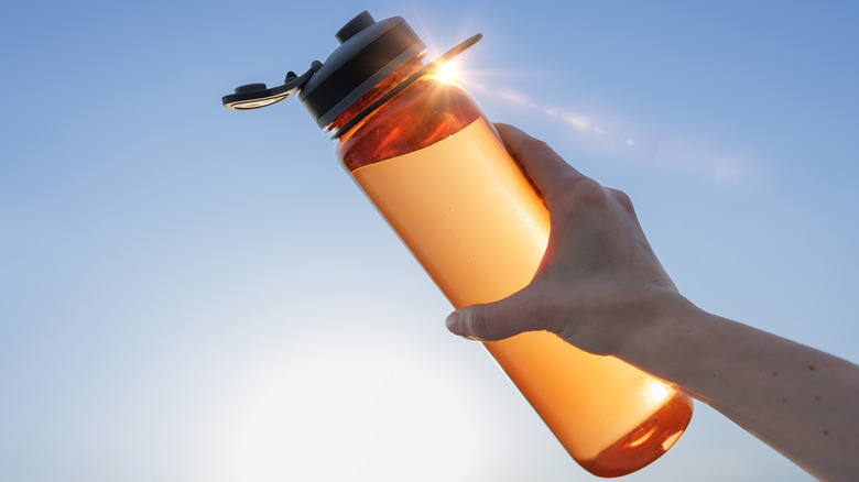 Hand holding an orange glass reusable water bottle.