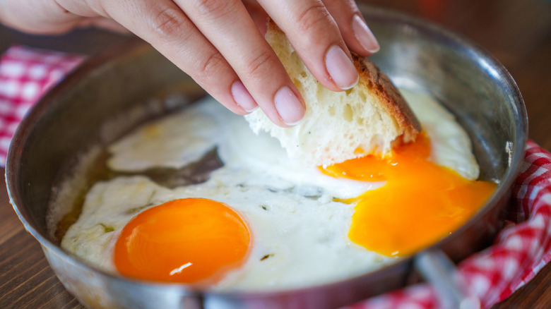 A hand dips bread into fried eggs