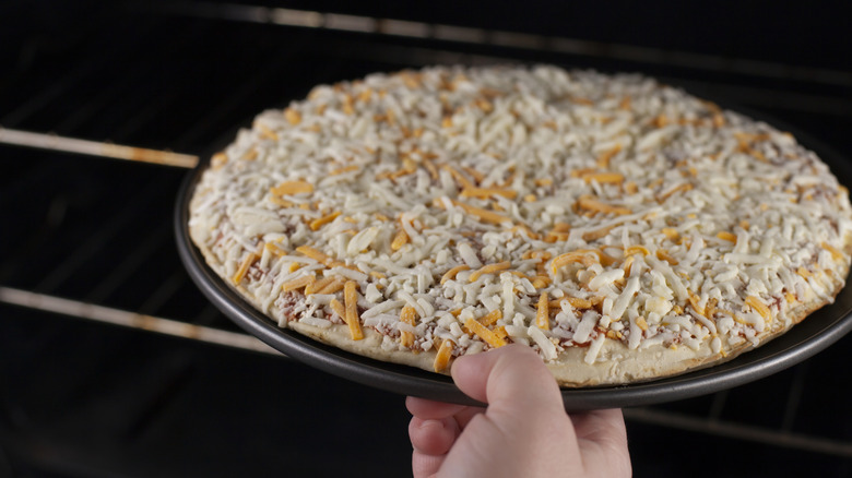 Close-up of a hand putting a frozen pizza into the oven
