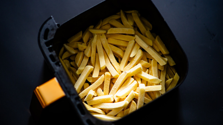A black air fryer basket filled with frozen french fries.