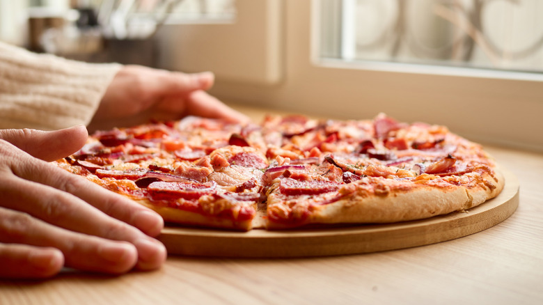 Hands holding a pepperoni pizza on a serving platter
