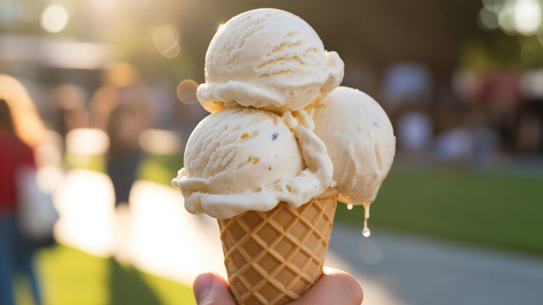 A hand holding a cone with three scoops of vanilla ice cream