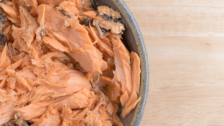 A close-up view of an opened can of salmon on a wooden table.