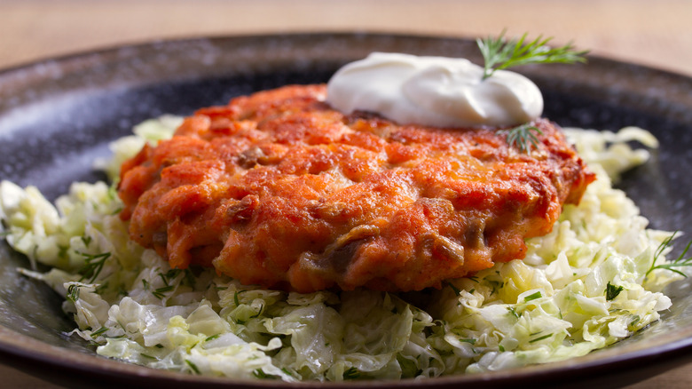 A perfectly seared salmon patty on a bed of coleslaw topped with sour cream and a sprig of dill.