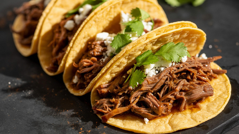 Four tacos filled with shredded beef and topped with white cheese and cilantro