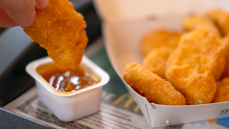 Hand dipping McDonald's chicken nugget into sauce.