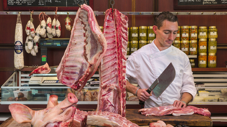 A butcher is seen handling a cut of meat with several others also in the frame.