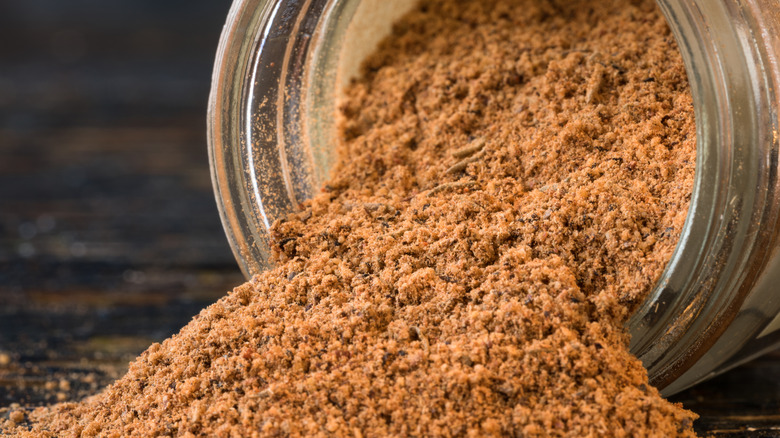 Jerk seasoning is spilling from a glass jar