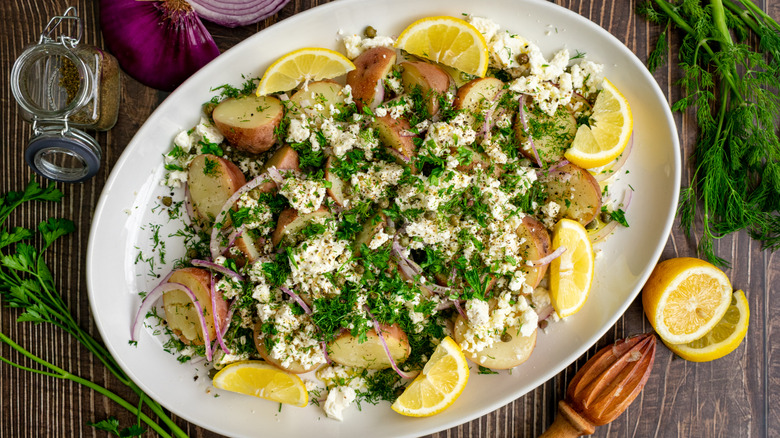 Potato salad with herbs, red onion, and a creamy cheese topping on a platter