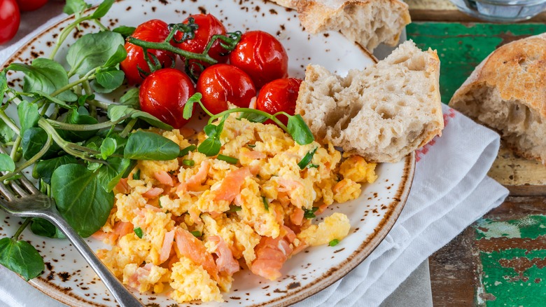Scrambled eggs and smoked salmon, greens, tomatoes and bread.