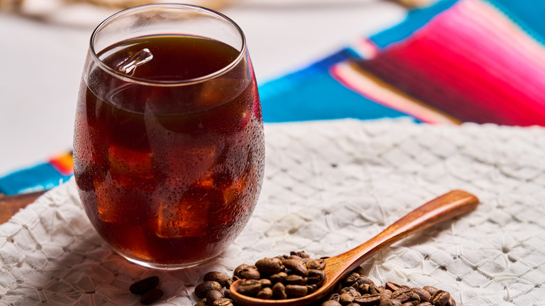 A glass of cold brew with ice and a wooden spoon with coffee beans