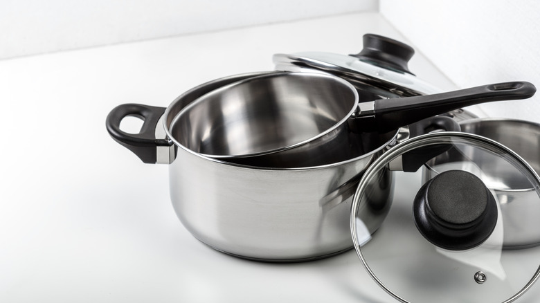 Stainless pots and a pan with lid against an off-white background