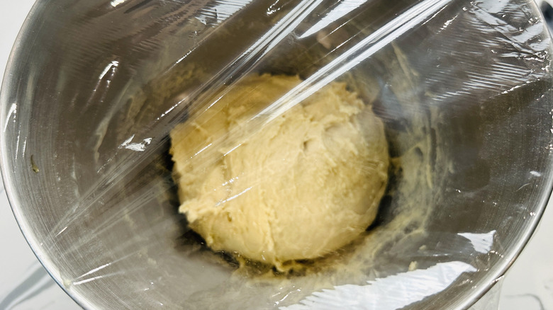 dough in a plastic wrap-covered metal bowl