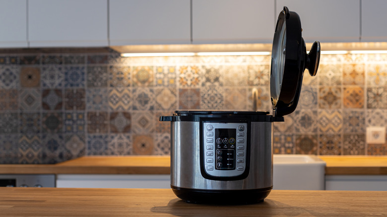 Opened pressure cooker on wooden counter in modern kitchen.
