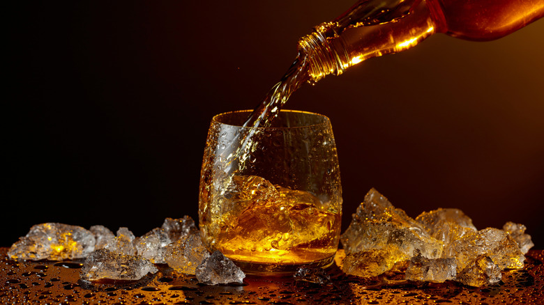 Pouring whiskey into glass with ice