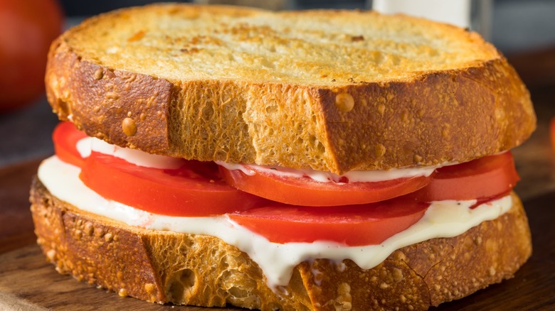 A halved tomato sandwich with its ingredients also in the frame.