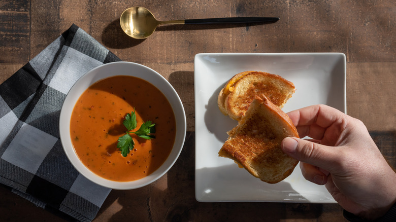 A bowl of tomato soup with a grilled cheese on the side.