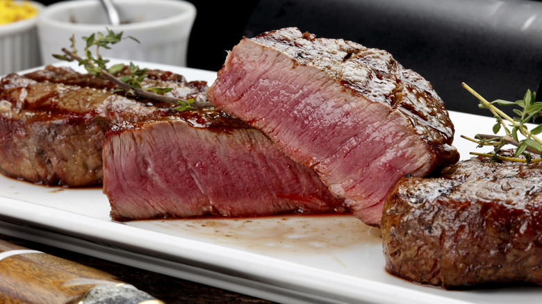 Three sirloin steaks on a long white plate, the one in the center is cut in half to show a rare center