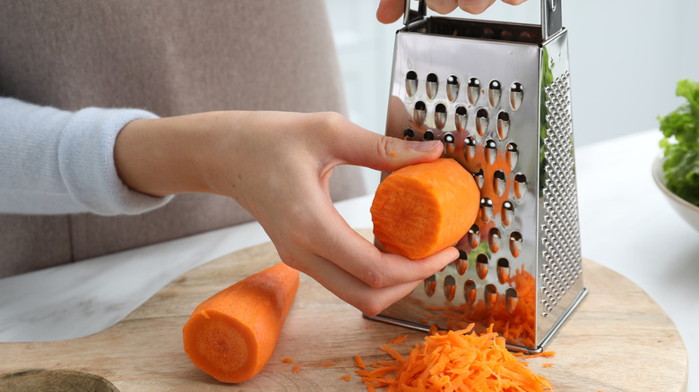 Person grating a carrot with a box grater