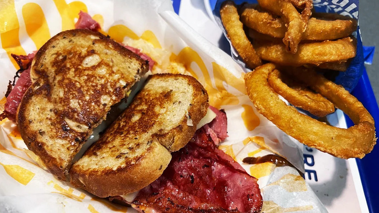 Culver's Grilled Reuben Melt in a tray alongside a side order of onion rings