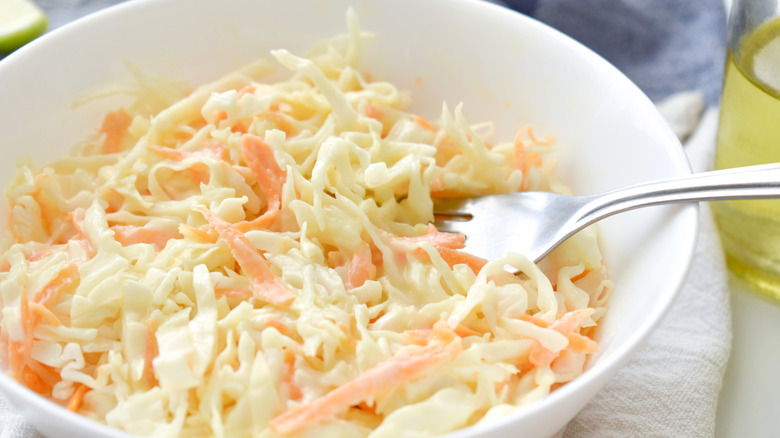A close-up of a bowl of simple, crunchy coleslaw with shredded cabbage and carrots with a fork in it.