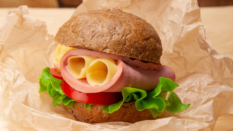 A simple ham and cheese sandwich (with lettuce and tomatoes) on a roll on top of butcher paper.