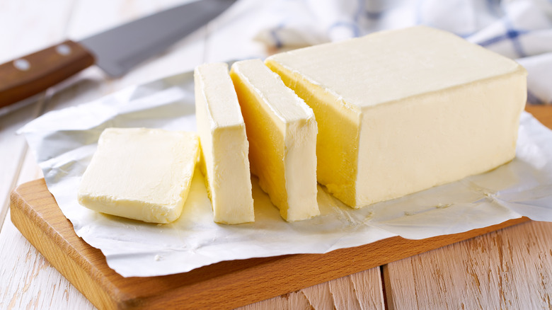 A stick of butter with some slices pre-cut on a cutting board
