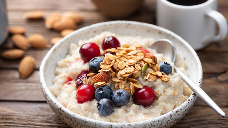 Oatmeal porridge bowl with berries, crunchy granola topping, cup of black coffee on rustic wooden table background, closeup view.
