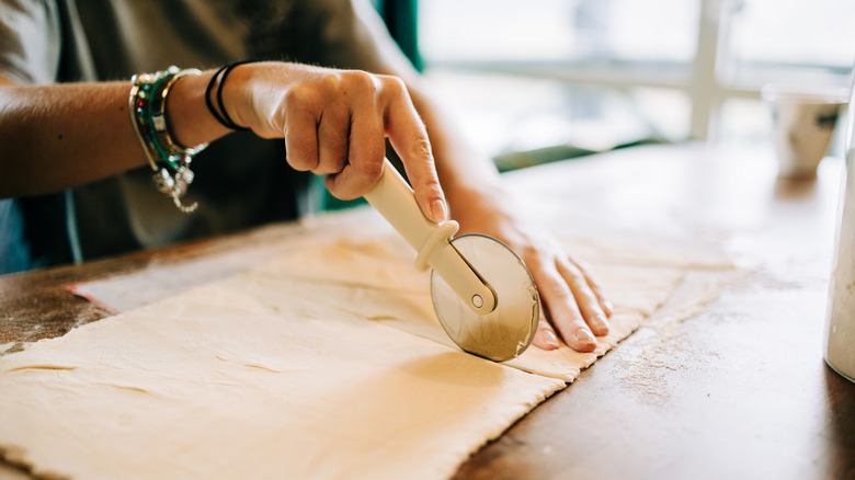Person cutting pie dough with a pastry wheel.