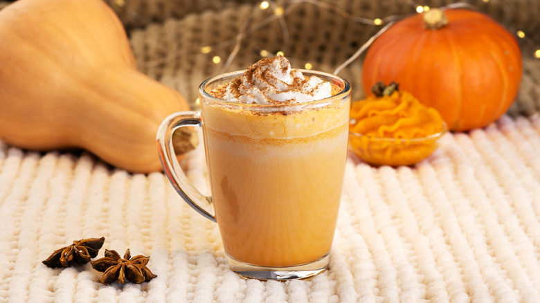 Cup of pumpkin spice latte with spices and whole squashes in the background