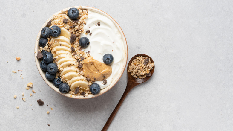 Yogurt bowl with fruit and peanut butter next to spoon on gray counter.