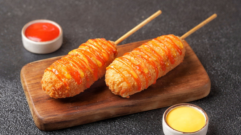 Two corn dogs arranged on a cutting board with sauces