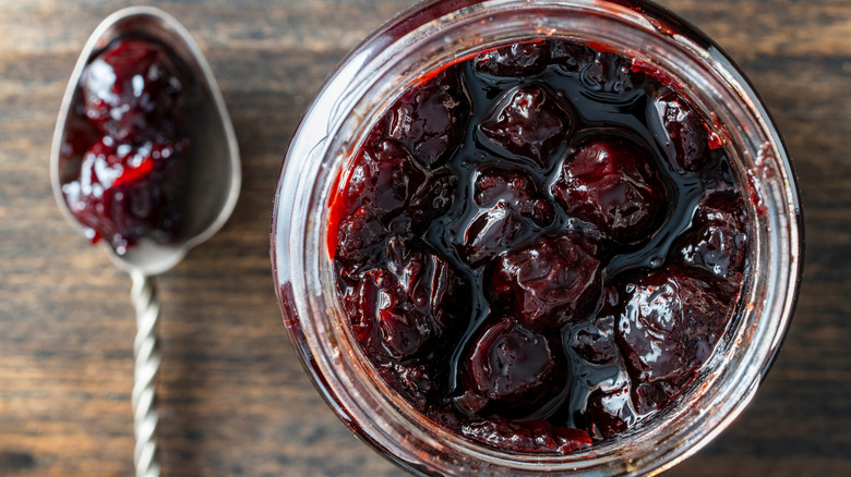 A glass jar and spoon full of red cherry jam
