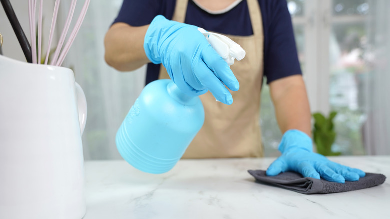A person wearing blue gloves and spraying a marble countertop with cleaning solution
