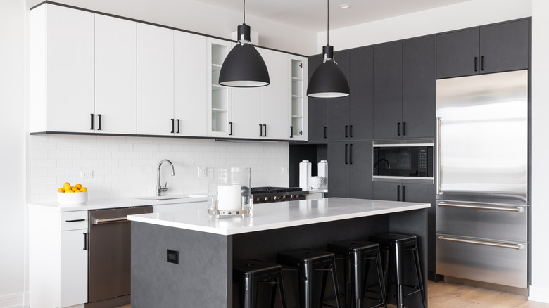 A modern kitchen with a marble-topped island, black and gray cabinets, and black hanging lamps