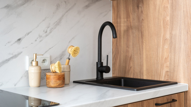 A marble counter with various cleaning supplies on it next to a sink with black fittings
