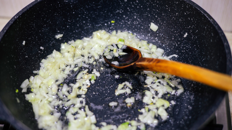 Onions sautéing in a deep skillet with wood spoon.