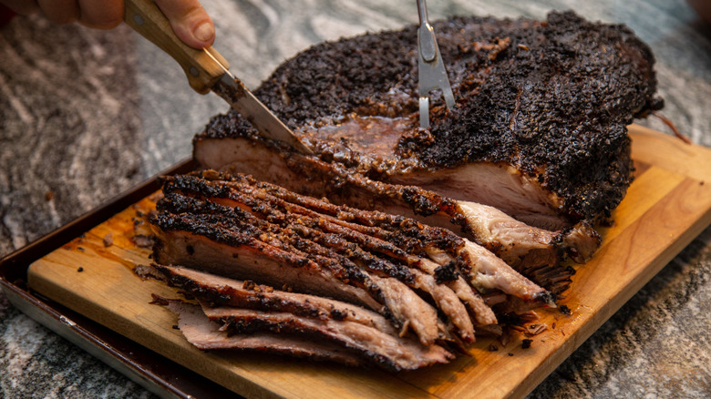 Person slicing cooked brisket on a cutting board.