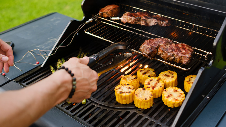 A person's hand tending grill with meat and veggies