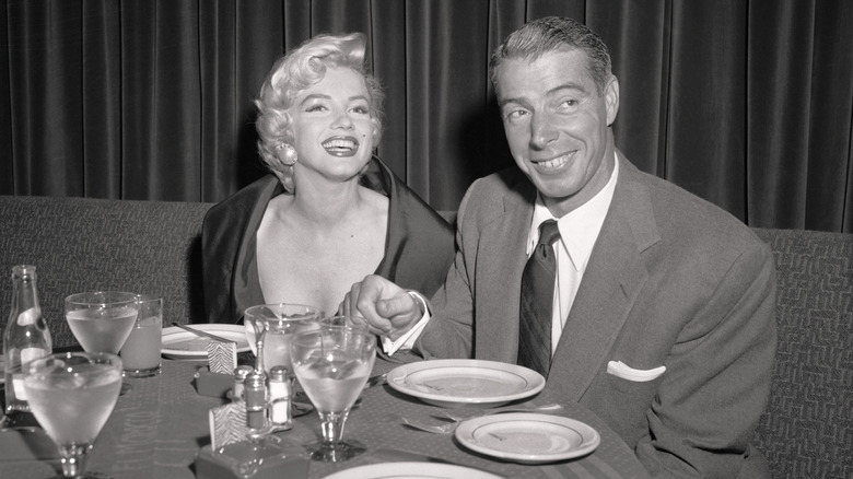 Black and white photo of Joe DiMaggio and Marilyn Monroe sitting together at a dinner table